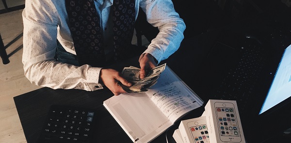 Canva - Person Counting Money With Smartphones in Front on Desk